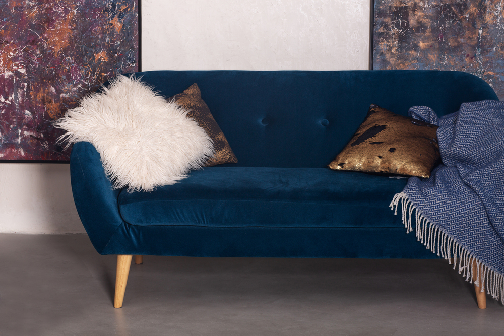 Sofá de terciopelo azul petróleo, ideal para agregar un toque de lujo y modernidad a cualquier sala, complementado con detalles acogedores y artísticos.